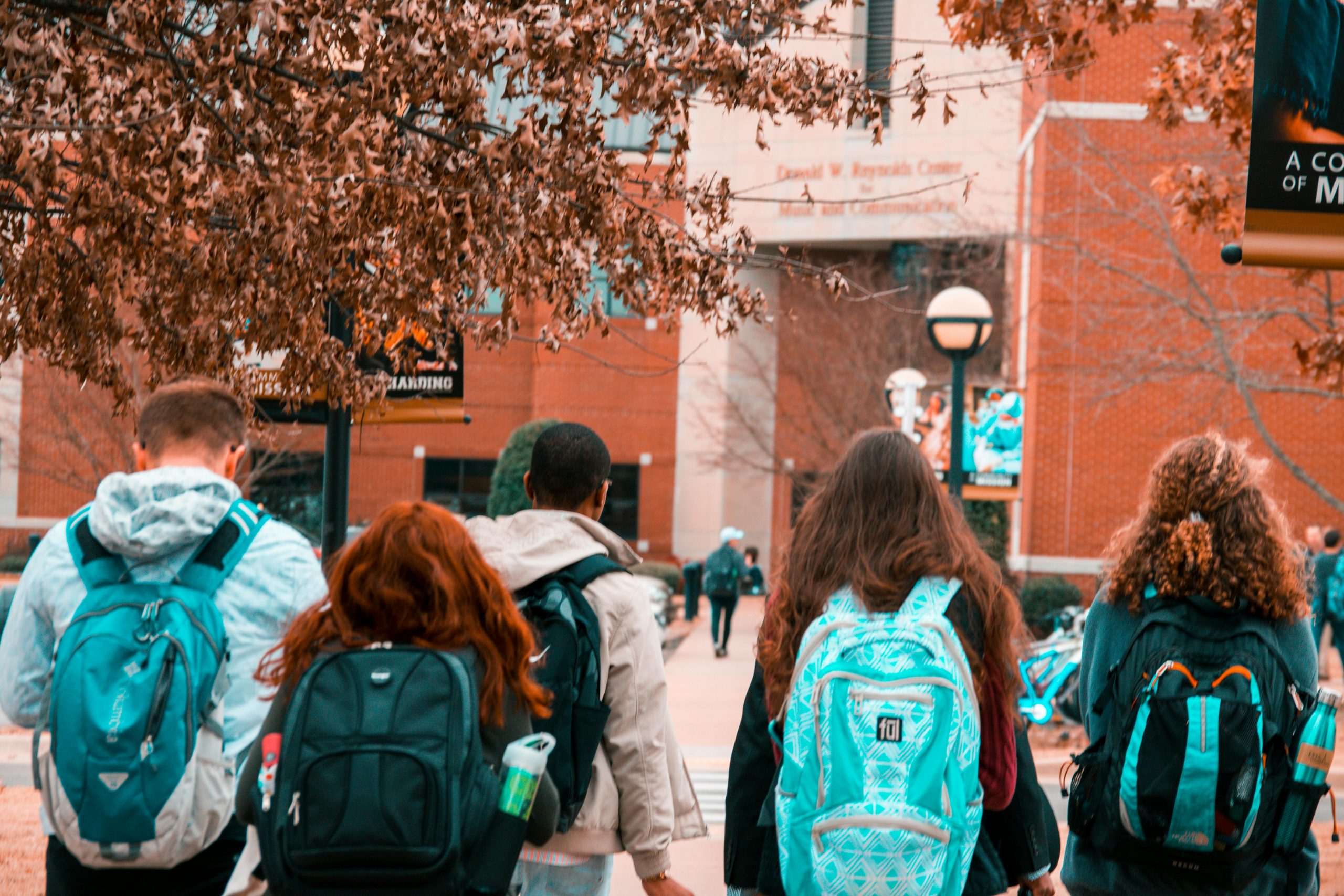 Students wearing backpacks walking toward a building on college campus