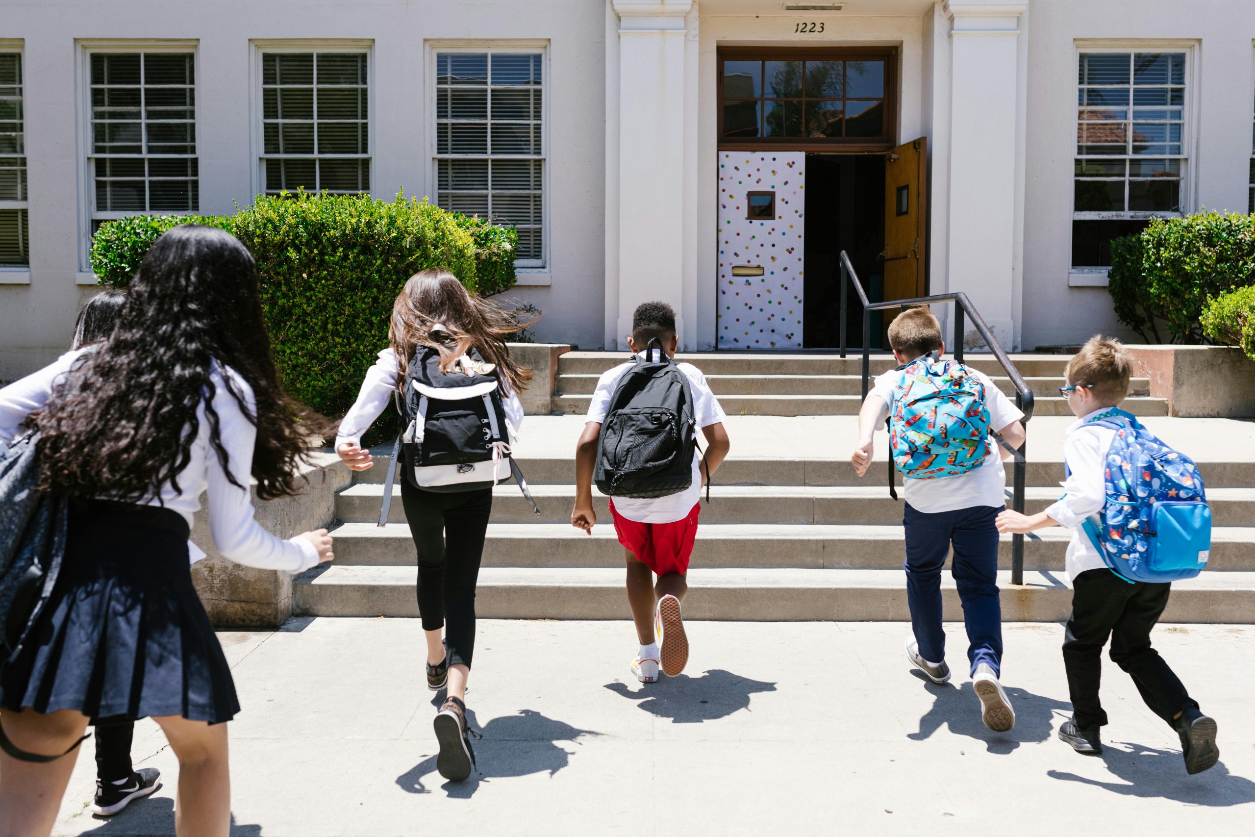 Students wearing backpacks running toward the front door of the school